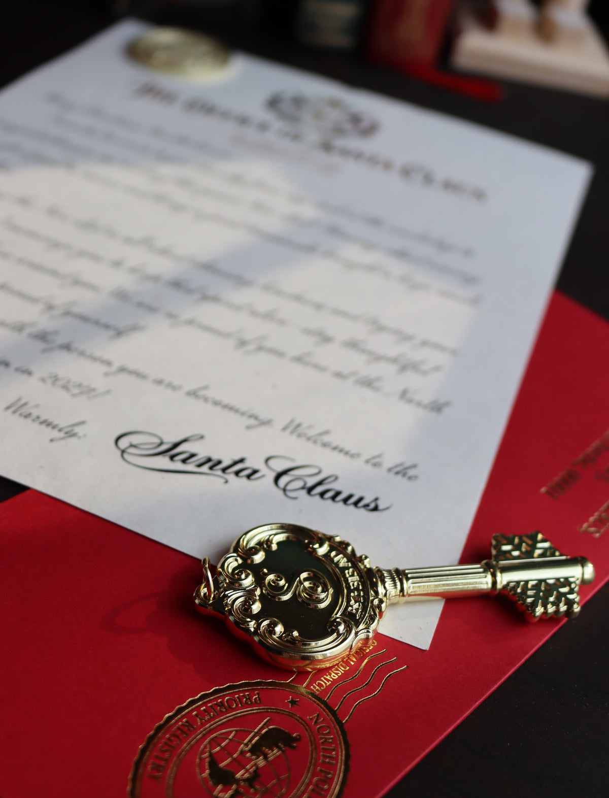 A decorative antique-style gold key with a green enamel center rests on a red envelope next to a printed Santa Claus invitation card.