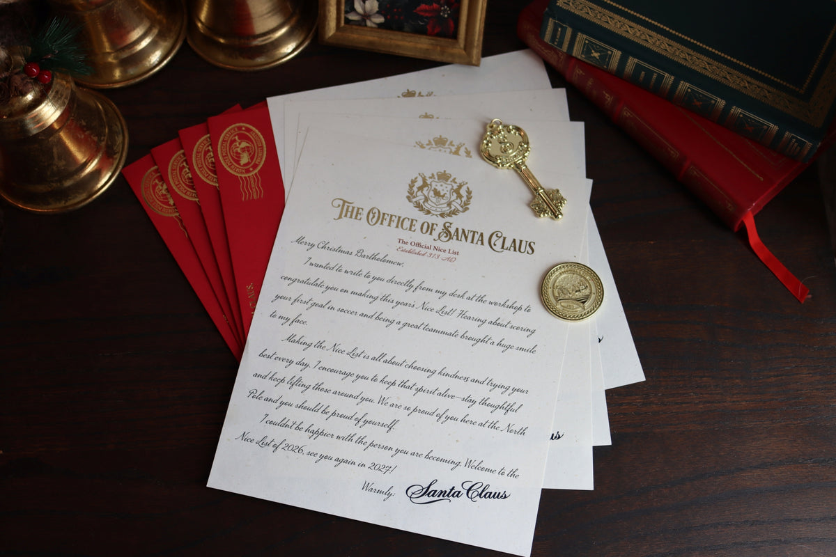 A Santa Claus themed letter from 'The Office of Santa Claus' displayed on a dark wooden table, surrounded by red envelopes, a brass bell, a gold key, and a gold seal.
